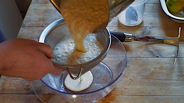 Pouring hand-mashed oats through a sieve to make oat milk