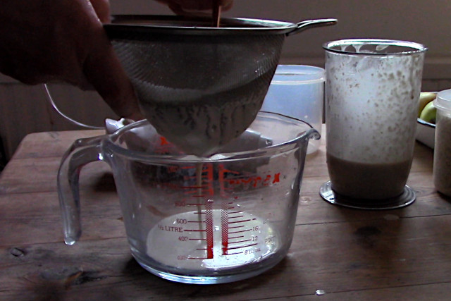 Straining the mashed oats through fine-mesh metal sieve